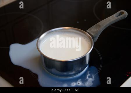 Pose à plat d'une casserole avec du lait bouilli qui s'est renversée sur une table de cuisson à induction avec verre noir Banque D'Images