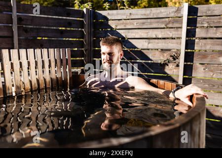 Jeune homme appréciant dans le bain à remous extérieur. Concept glamping et relaxation. Banque D'Images