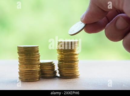 Main mettant la pièce d'or sur une pile de pièces. Concept de richesse et d'espace de copie. Banque D'Images