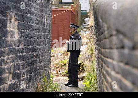 La police devant l'arrière d'une maison dans Minnie Street, alors que la police du West Yorkshire a déclaré qu'un certain nombre de mandats avaient été exécutés dans la zone Keighley de Bradford pendant la nuit en relation avec l'incendie mortel du 21 août. Deux autres personnes ont été arrêtées sur suspicion de meurtre suite à l'incendie de la maison qui a tué une mère et trois enfants à Bradford. Date de la photo : samedi 24 août 2024. Banque D'Images