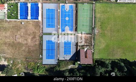 Vue aérienne révélant un éventail de courts de tennis et de basket-ball d'un bleu vif, complétés par des champs verdoyants, le tout dans un ciel dégagé. Banque D'Images