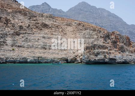 Bateau de pêcheurs ancré près d'une falaise dans le fjord accidenté de Musandam, Sultanat d'Oman Banque D'Images