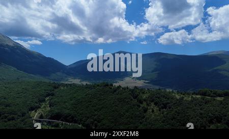 De vastes collines verdoyantes s'étendent à travers la campagne, embrassées par des nuages moelleux au-dessus de vous, créant un tableau serein et pittoresque de la beauté de la nature. Banque D'Images