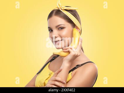 Portrait d'une belle fille brune avec une peau saine et propre et maquillage frais sur un fond jaune. Elle tient une banane. Concept de nutrition saine. Banque D'Images