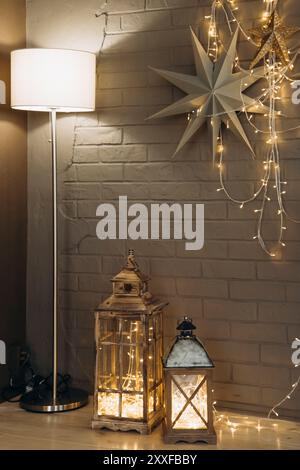 Décor de vacances rustique avec deux lanternes remplies de guirlande lumineuse, debout à côté d'un lampadaire moderne et des ornements d'étoiles contre un mur de briques pour un Banque D'Images