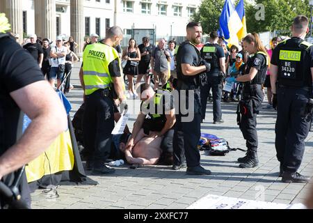 Berlin, Allemagne, 24 août 2024. Cette image montre des officiers de police berlinois qui arrêtent un homme lors d'un événement du jour de l'indépendance ukrainienne près de la porte de Brandebourg. L'individu, qui portait un couteau, s'était blessé avant d'être soumis aux forces de l'ordre. Des agents sont vus en train de sécuriser le suspect sur le terrain et de préparer une aide médicale à côté d'un véhicule de police, tandis que des spectateurs et du matériel de l'événement sont visibles en arrière-plan de l'opération de sécurité dans la capitale. Felix Wolf/Alamy Live News Banque D'Images