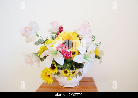 Photo horizontale de studio de natures mortes d'un vase avec des fleurs scéniques en plastique jaune et blanc devant un mur blanc. Arrangement pour tournesol printanier. Banque D'Images