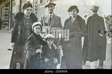 Novi Sad, Yougoslavie (aujourd'hui Serbie) - 1939 : groupe d'adultes avec des enfants posant pour la photographie dans la rue avec le policier (bras de gendarme) passant Banque D'Images