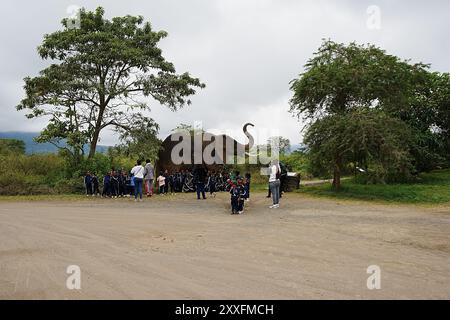 ARUSHA, TANZANIE - 19 juillet 2024 : groupe scolaire devant un éléphant artificiel à l'entrée du parc national africain, ciel nuageux dans la chaude journée d'hiver. Banque D'Images