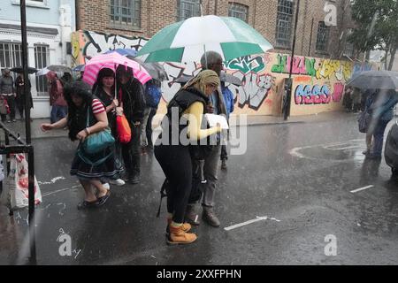 Des gens à l'abri de la pluie à Notting Hill, à l'ouest de Londres. Le week-end du jour férié du mois d'août s'est bien amorcé et les températures ont été décevantes. Date de la photo : samedi 24 août 2024. Banque D'Images