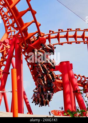 Energylandia, Pologne - 23 août 2024 : une image en gros plan d'une piste de montagnes russes rouge et du ciel bleu et des gens excités qui apprécient la balade. Banque D'Images