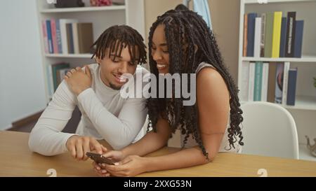 Un couple souriant s’assoit étroitement dans leur salon, partageant un moment sur un smartphone. Banque D'Images