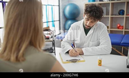 Un médecin masculin rédige des notes lors d'une consultation avec une patiente dans une salle de clinique lumineuse. Banque D'Images