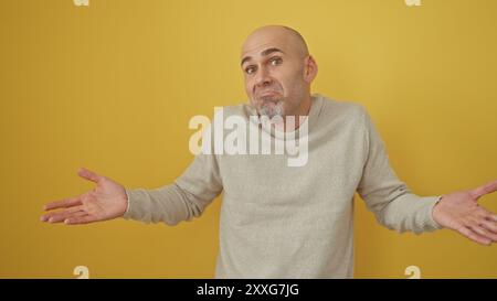 Bel homme chauve avec barbe dans des gestes de pull sur fond jaune Banque D'Images