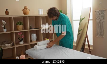 Jeune homme disposant des serviettes dans une salle de thérapie spa sereine avec des plantes en pot et des décorations élégantes Banque D'Images