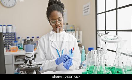 Une scientifique afro-américaine mène des expériences dans un laboratoire intérieur, entouré d'équipements de chimie. Banque D'Images