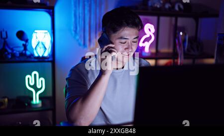 Un jeune homme asiatique parlant au téléphone dans une salle de jeux éclairée au néon la nuit Banque D'Images