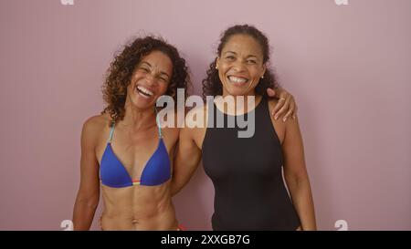 Deux femmes latines adultes heureuses s'embrassent devant un mur rose, exprimant l'amour et la proximité en tant qu'amies ou sœurs. Banque D'Images