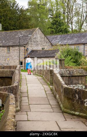 Femme marchant sur Holme Bridge, le vieux pont médiéval en pierre de packhorse sur la rivière Wye dans la ville de marché Peak District Derbyshire de Bakewell Banque D'Images