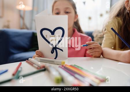 Enfants créant la main carte de fête des pères avec des marqueurs et des crayons de couleur sur la table avec message d'amour sur la carte. Activité réconfortante montrant la créativité et l'affection des enfants Banque D'Images