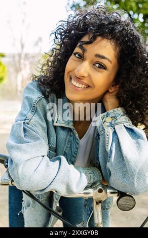 Portrait d'une jeune femme joyeuse à vélo souriant à l'appareil photo du parc de la ville Banque D'Images