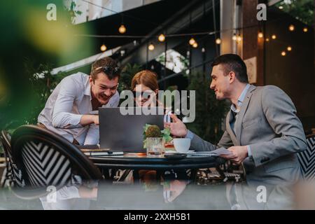 Les gens d'affaires collaborent en extérieur tout en étant engagés dans une discussion animée sur un ordinateur portable lors d'une réunion informelle dans un environnement de café détendu. Banque D'Images