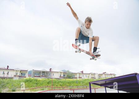 Jeune skateboarder intense en saut en hauteur contre le ciel et les zones de couchage Banque D'Images