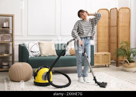 Jeune femme portant des écouteurs nettoyage tapis avec aspirateur dans le salon Banque D'Images