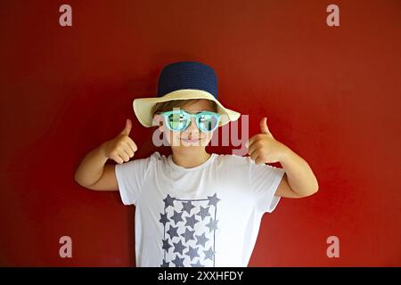 Très emothional enfant porter un chapeau et des lunettes de soleil sur fond rouge. Copie espace, lumière du jour Banque D'Images