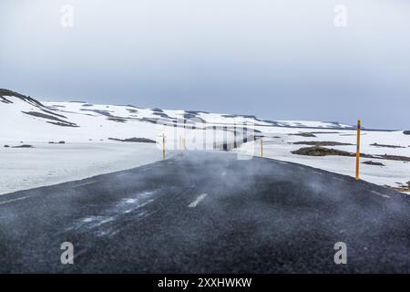 Une traînée de brouillard se déplace le long d'une route goudronnée courbe traversant un paysage enneigé Banque D'Images