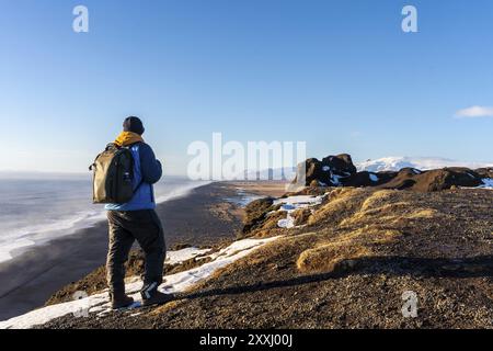 Un touriste avec le dos tourné au point de vue de la plage de Dyrholaey dans l'hiver froid avec de la neige en Islande Banque D'Images