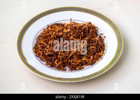 Oignons frits croustillants maison ou peyaj beresta sur une plaque blanche sur une surface en bois clair. Un aliment de base traditionnel de la cuisine bangladaise, fait avec du minces Banque D'Images