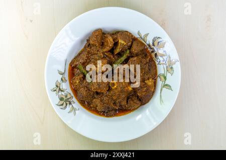 Délicieux curry de mouton dans une plaque en céramique blanche sur fond de bois. Le mouton bhuna est un plat bangladais populaire, savoureux et épicé. Vue de dessus. Banque D'Images