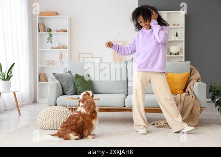 Adolescente afro-américaine dans des écouteurs jouant avec le cavalier mignon King Charles spaniel à la maison Banque D'Images