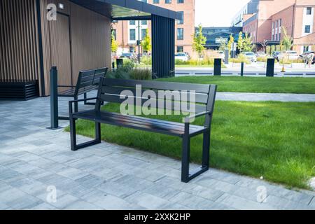 Vue en perspective du chemin pavé avec pelouse verte, herbe décorative et bancs en bois modernes devant des bacs de gabion en fil de fer et remplis de Banque D'Images