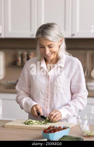 Femme souriante hachant du concombre frais pour la salade Banque D'Images