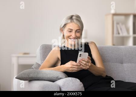 Femme souriante utilisant un smartphone moderne à la maison Banque D'Images