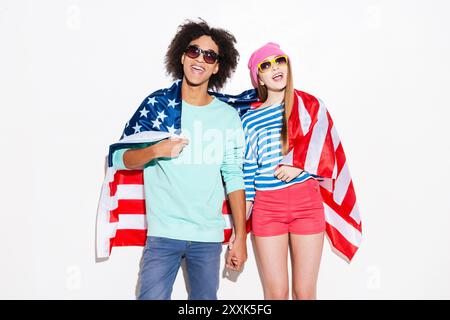 Insouciant et amoureux. Jeune couple funky couvert de drapeau américain et souriant tout en se tenant sur fond blanc Banque D'Images