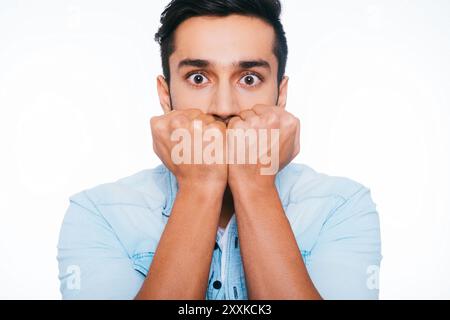 Se sentir choqué et terrifié. Jeune homme indien terrifié tenant les poings près du visage et vous regardant tout en se tenant debout sur fond blanc Banque D'Images