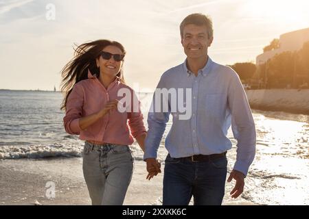 Couple profitant du coucher du soleil se promener le long de la plage tout en se tenant la main Banque D'Images