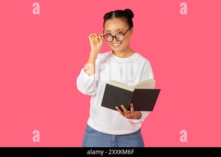 Jeune femme lisant le livre tout en souriant sur un fond rose Banque D'Images