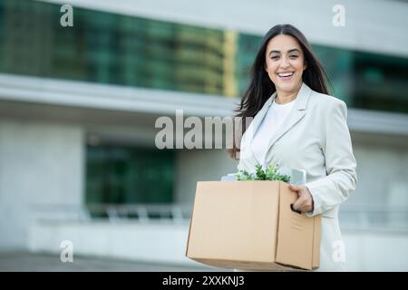 Jeune femme en costume blanc portant boîte de biens Banque D'Images