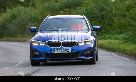 Whittlebury, Northants., UK - 25 août 2024 : 2022 bleu BMW 330e M sport hybride voiture électrique conduisant sur une route de campagne britannique. Banque D'Images