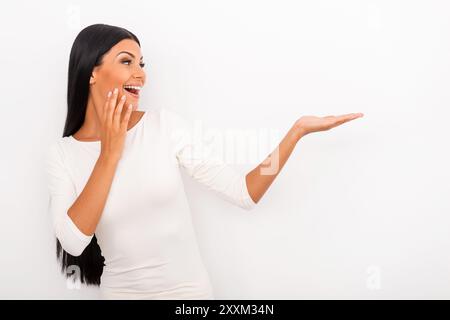 C'est tout simplement incroyable ! Jeune femme joyeuse tenant l'espace de copie sur sa main et le regardant tout en se tenant debout sur fond blanc Banque D'Images