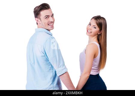 Profiter de leur temps ensemble. Vue arrière du beau jeune couple aimant regardant par-dessus l'épaule à la caméra tout en se tenant sur fond blanc Banque D'Images