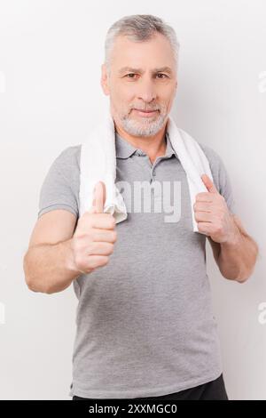 Gardez votre corps en forme. Homme senior confiant cheveux gris portant serviette sur les épaules et montrant son pouce vers le haut tout en se tenant debout sur fond blanc Banque D'Images