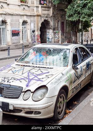 Tbilissi, Géorgie - 28 juillet 2024 : vieille voiture peinte abandonnée avec des fenêtres cassées dans la rue dans le centre de la ville de Tbilissi le jour couvert d'été, Géorgie Banque D'Images