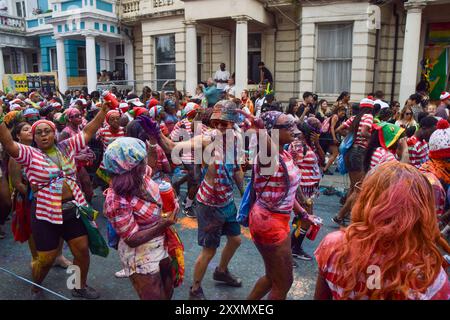 Londres, Royaume-Uni. 25 août 2024. Les fêtards habillés en personnage de livre de puzzle pour enfants Wally pulvérisent de la peinture colorée et de la poudre sur eux-mêmes et les spectateurs. Crédit : Vuk Valcic/Alamy Live News Banque D'Images