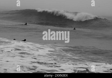 océan brumeux orageux avec peu de surfeurs le jour d'hiver en noir et blanc Banque D'Images