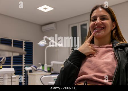 Adolescente souriant et montrant un doigt sur les bagues dentaires sur les dents, la fille est heureuse qu'elle aura des dents alignées. Conception des soins dentaires pendant la période Banque D'Images